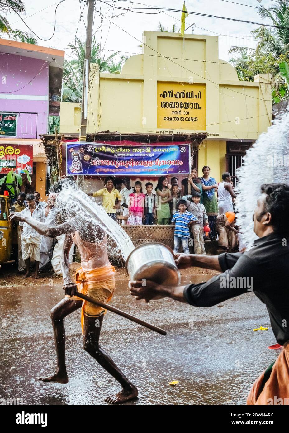 L'uomo balla in strada e fa oscillare un pipistrello per schioccare colorati palloncini d'acqua attaccati a una piramide simbolica oscillata da una corda e una puleggia, mentre i batteristi tengono il passo e i partecipanti giocosi schlashe Foto Stock