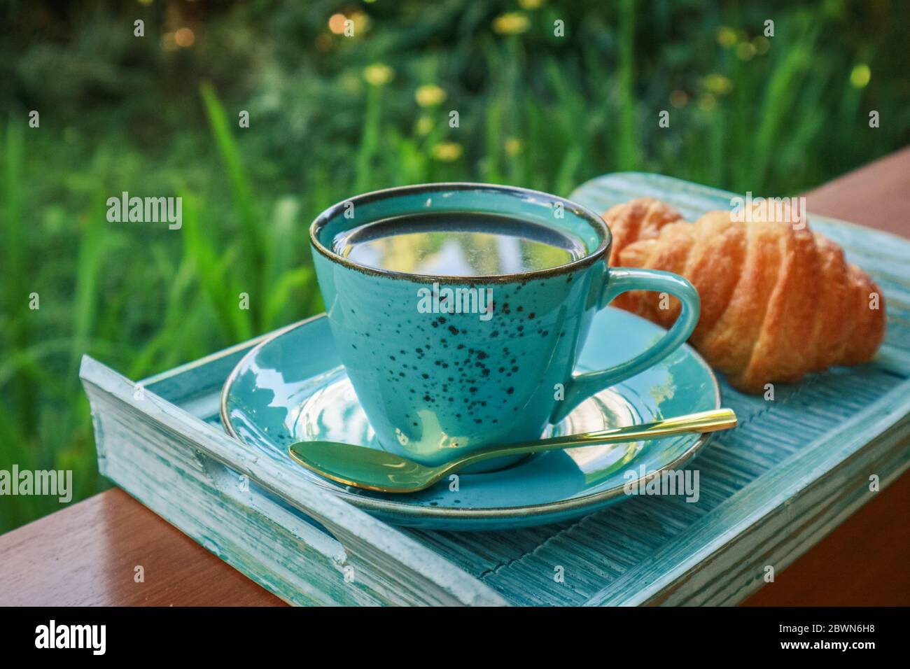 Tazza di caffè con croissant su vassoio di bambù blu all'aperto, guardaroba Foto Stock