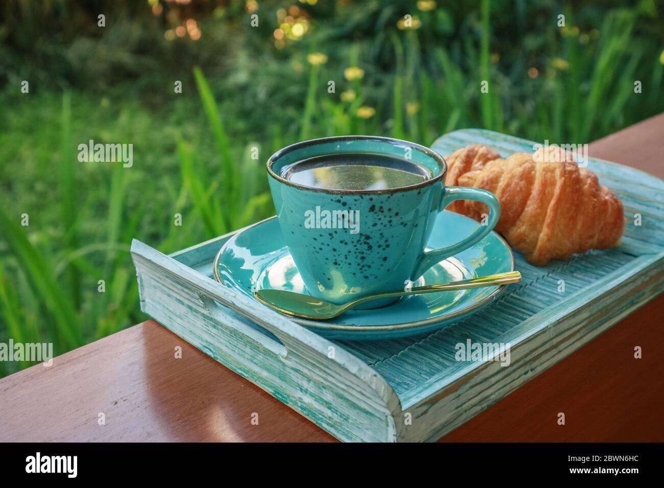 Tazza di caffè con croissant su vassoio di bambù blu all'aperto, guardaroba Foto Stock