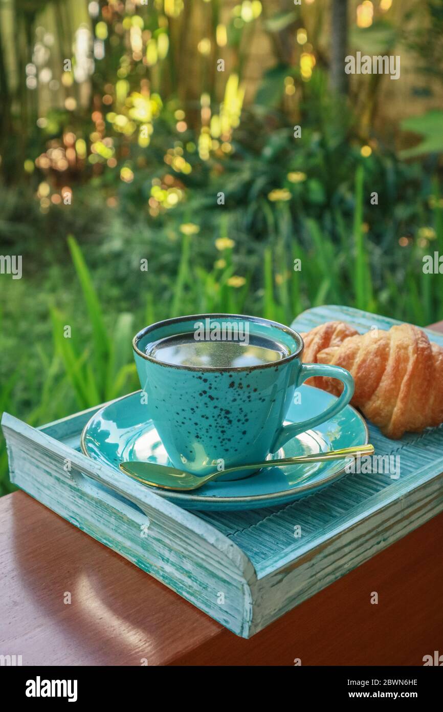Tazza di caffè con croissant su vassoio di bambù blu all'aperto, guardaroba Foto Stock