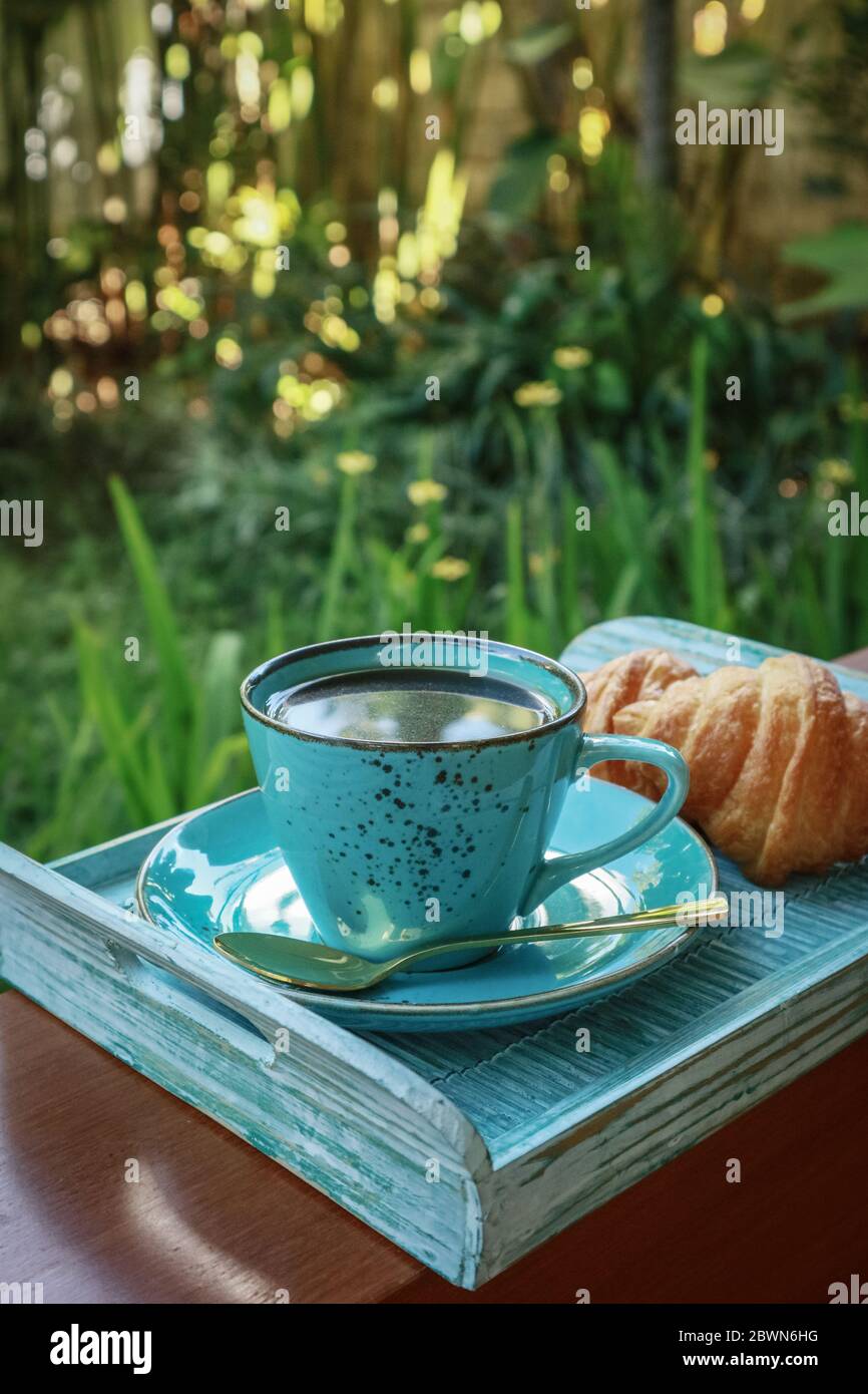 Tazza di caffè con croissant su vassoio di bambù blu all'aperto, guardaroba Foto Stock