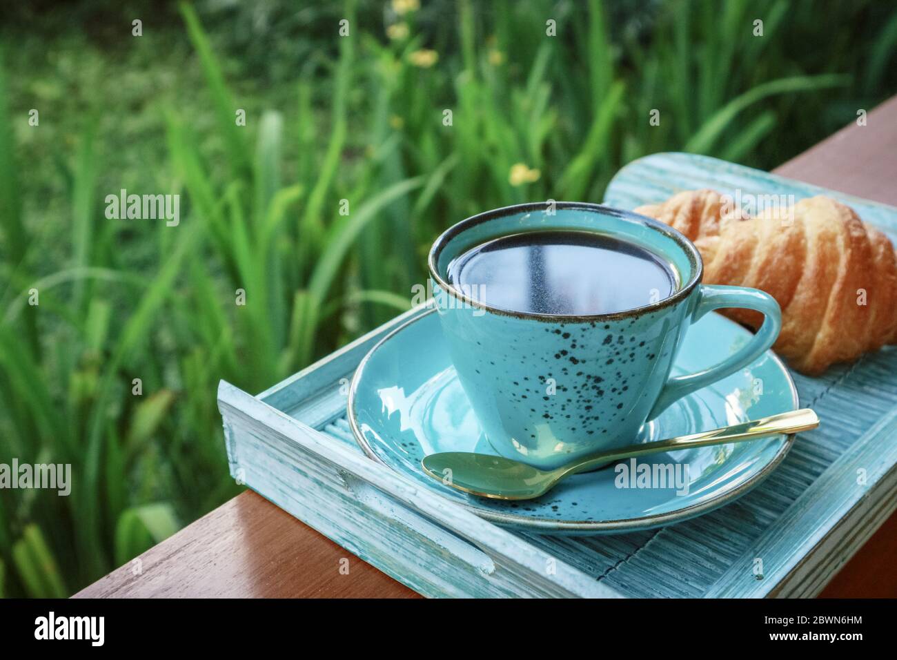 Tazza di caffè con croissant su vassoio di bambù blu all'aperto, guardaroba Foto Stock