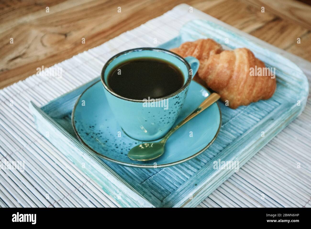 Tazza di caffè con croissant su vassoio di bambù blu all'aperto, guardaroba Foto Stock