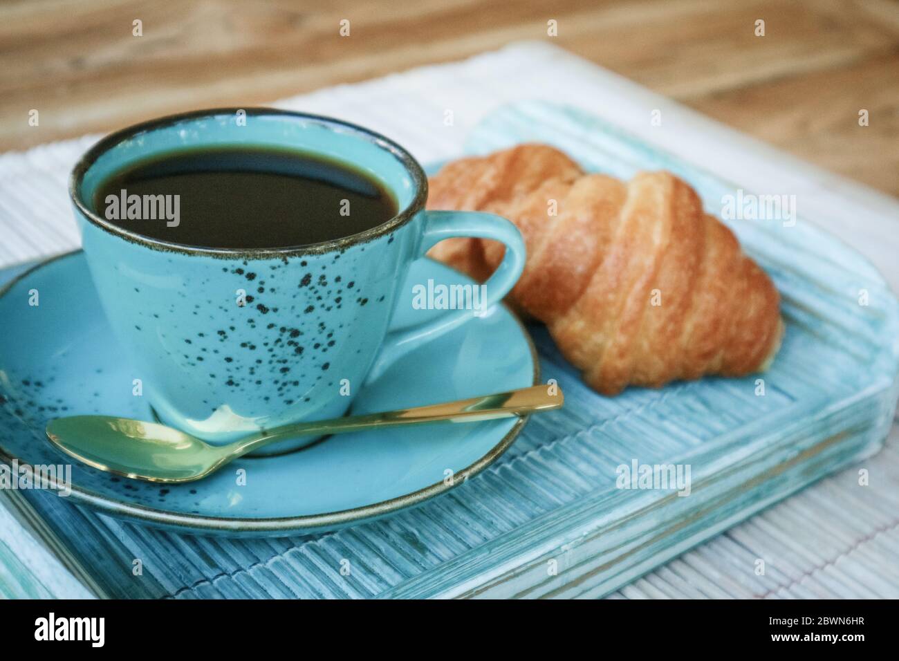 Tazza di caffè con croissant su vassoio di bambù blu all'aperto, guardaroba Foto Stock