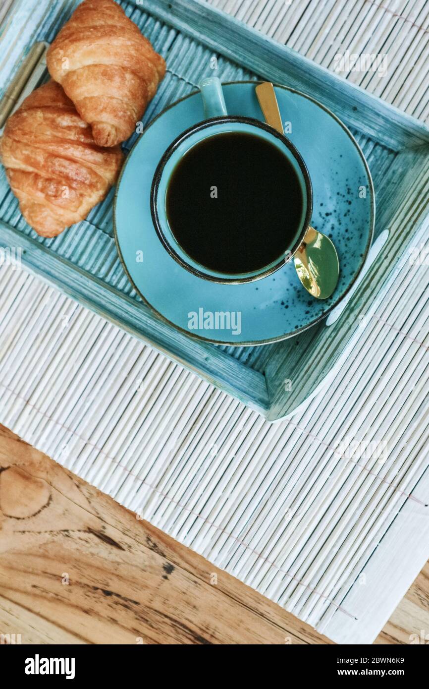 Tazza di caffè con croissant su vassoio di bambù blu all'aperto, vista dall'alto Foto Stock