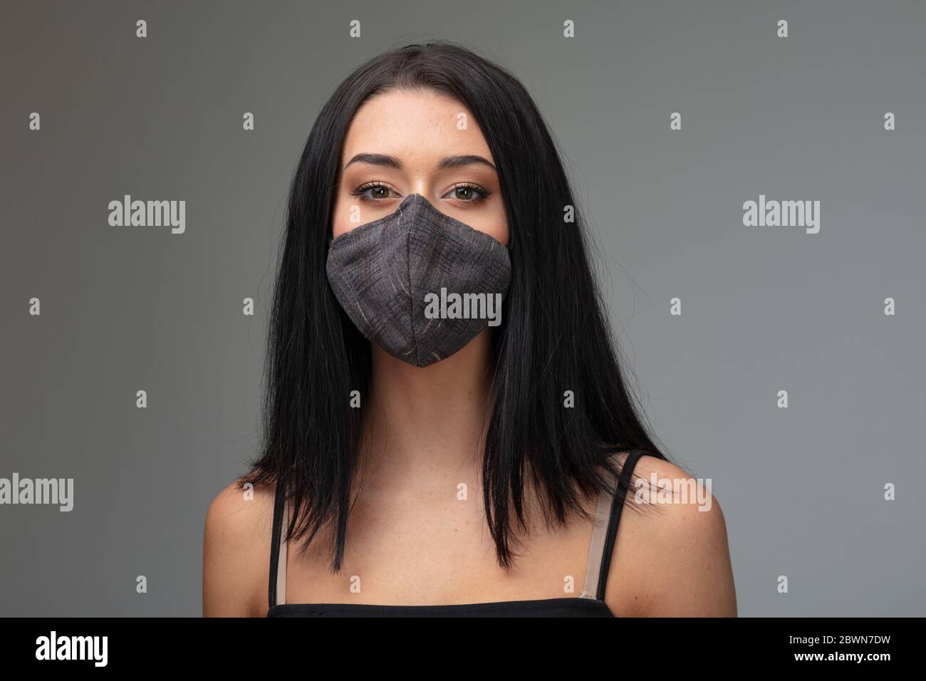 Giovane donna che indossa un elegante maschera nera sul viso su uno sfondo grigio concettuale del post Covid-19 stile di vita realtà in una testa e spalle Foto Stock