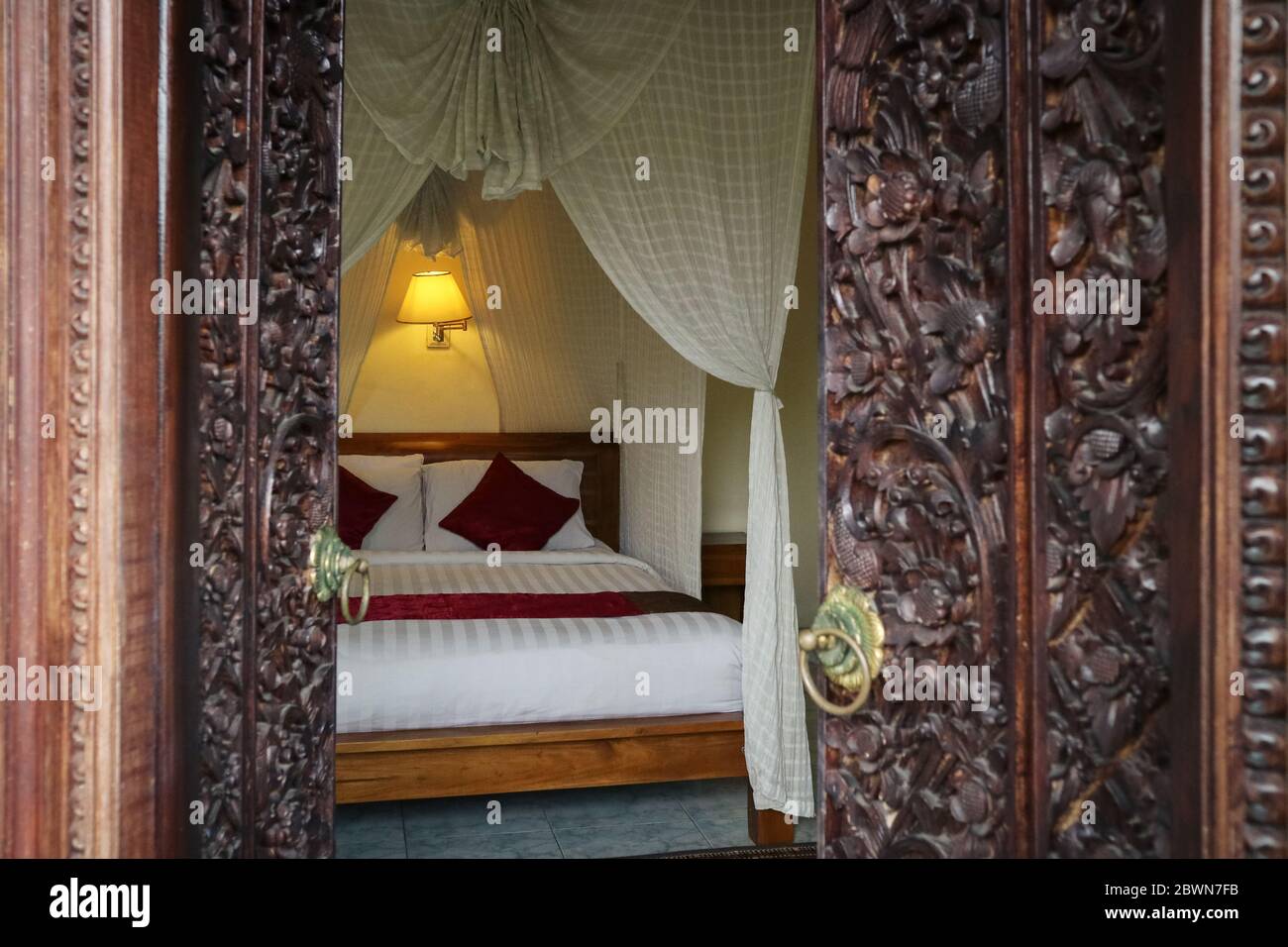 Letto tradizionale balinese con baldacchino. Vista attraverso l'apertura di porte scolpite. Foto Stock