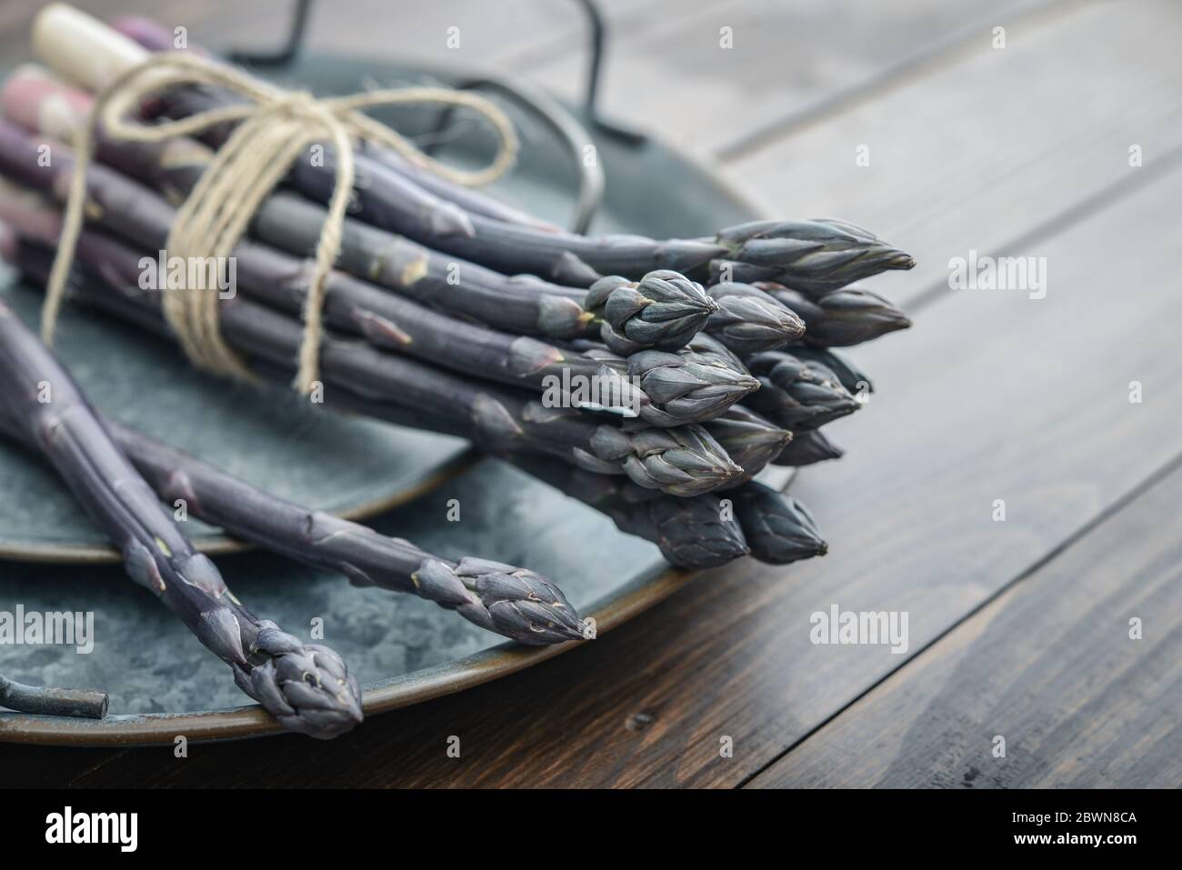 Un gambi commestibili e grezzi di asparagi su un vassoio su un chioseup di legno di fondo Foto Stock