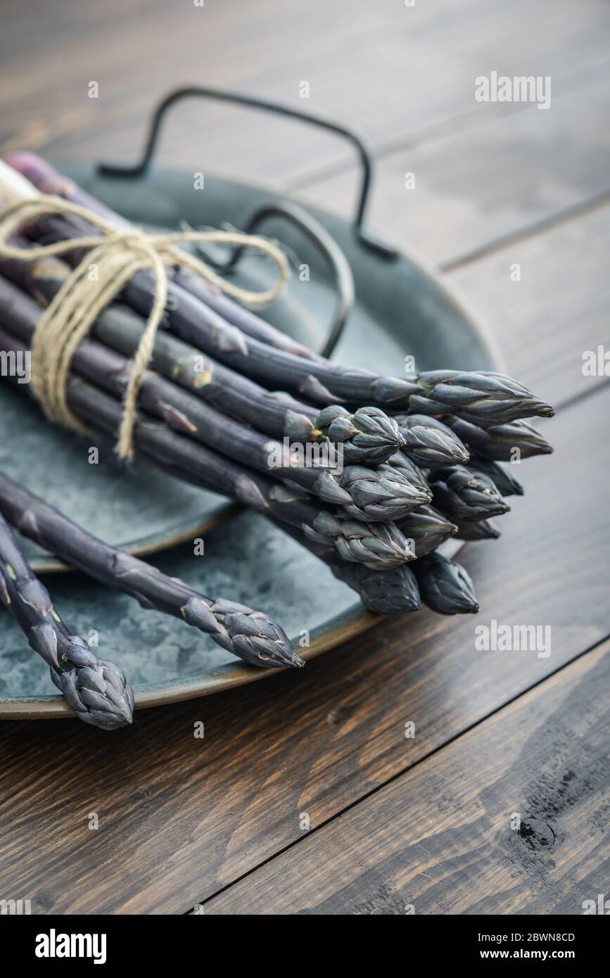 Un gambi commestibili e grezzi di asparagi su un vassoio su un chioseup di legno di fondo Foto Stock