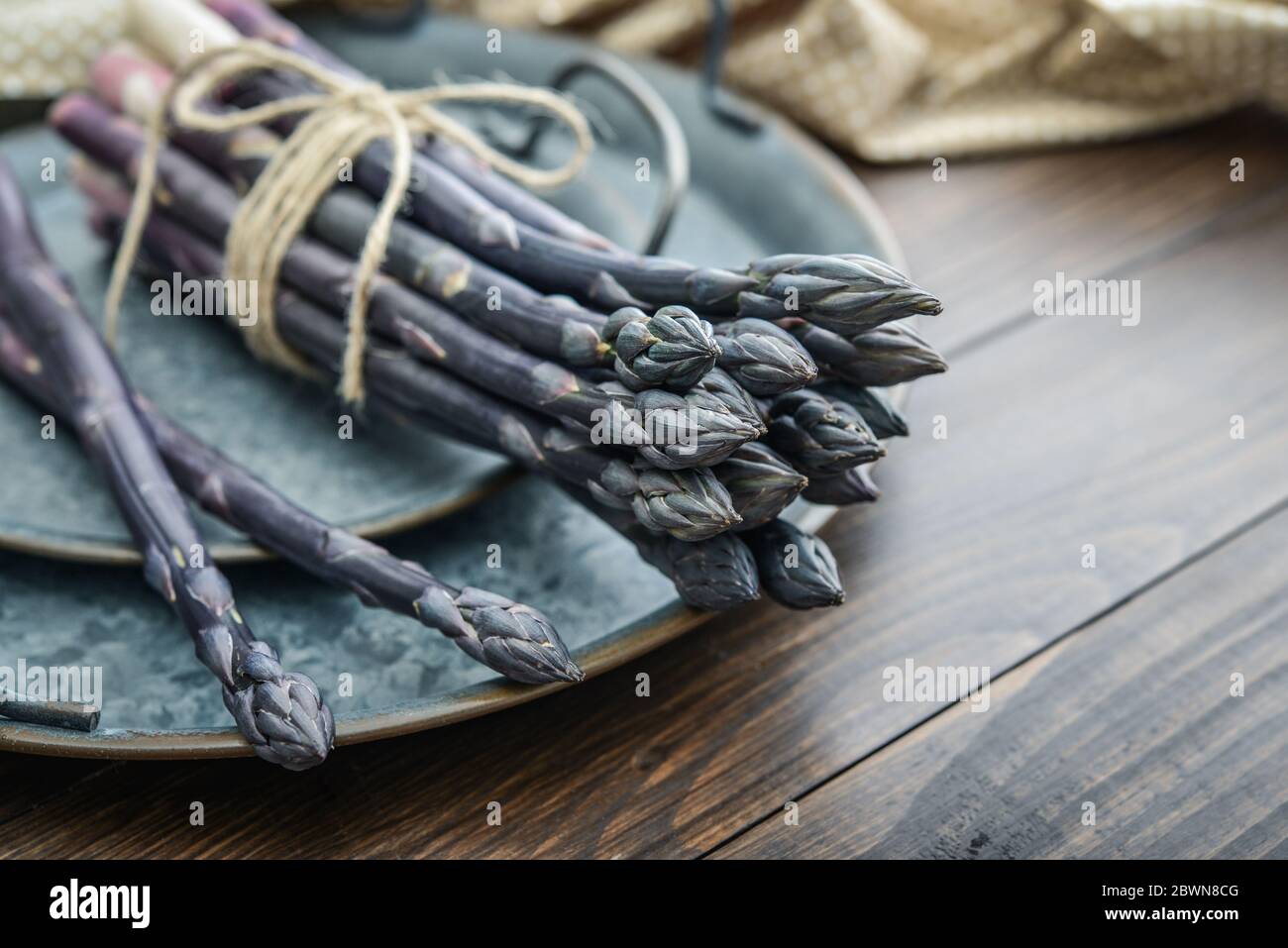 Un gambi commestibili e grezzi di asparagi su un vassoio su un chioseup di legno di fondo Foto Stock