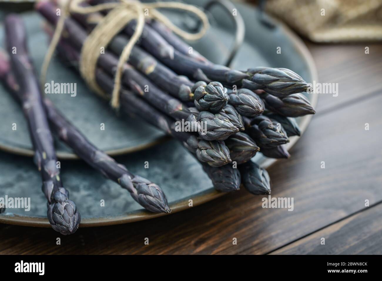 Un gambi commestibili e grezzi di asparagi su un vassoio su sfondo di legno, vista dall'alto Foto Stock