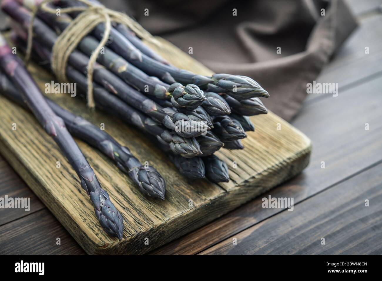 Un gambi commestibili e grezzi di asparagi su un vassoio su un chioseup di legno di fondo Foto Stock