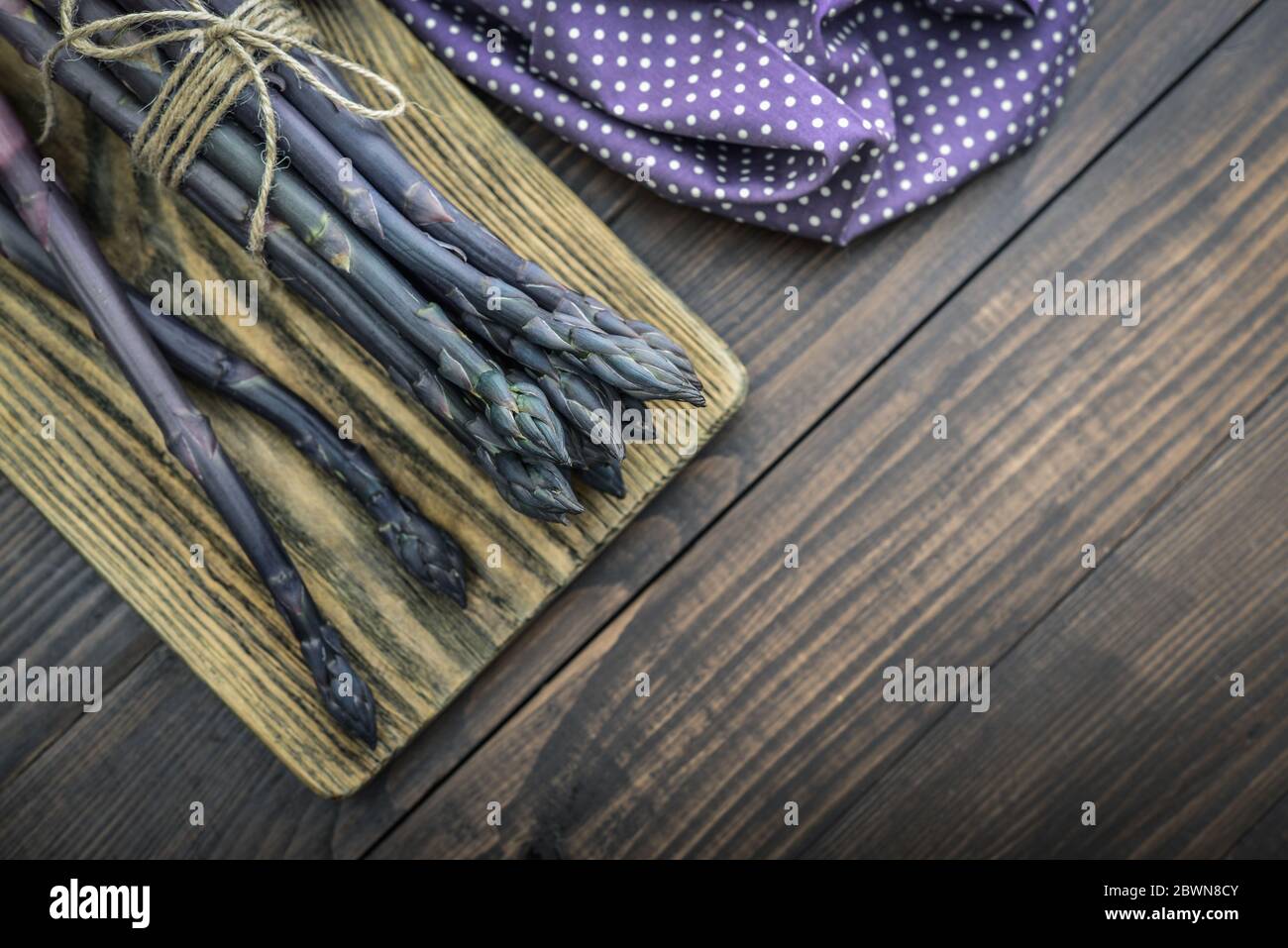 Un gambi commestibili e grezzi di asparagi su un vassoio su sfondo di legno, vista dall'alto Foto Stock