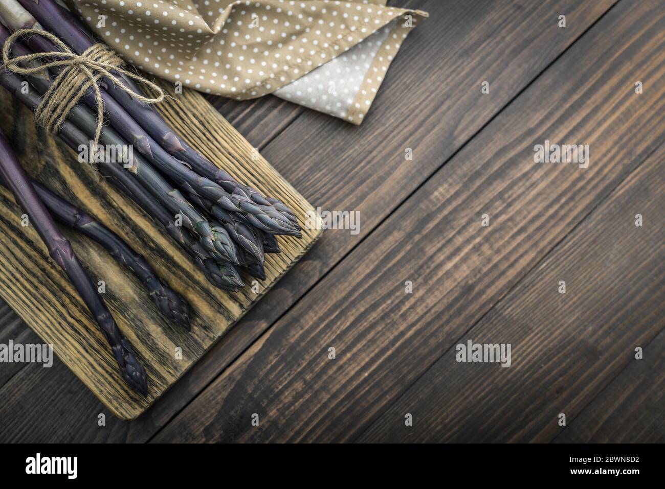 Un gambi commestibili e grezzi di asparagi su un vassoio su sfondo di legno, vista dall'alto Foto Stock