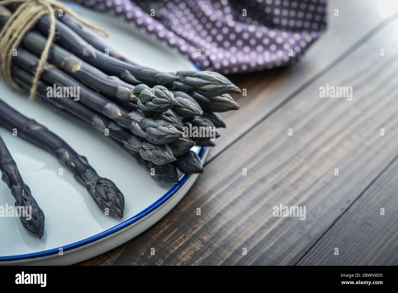 Un gambi commestibili e grezzi di asparagi su un vassoio su un chioseup di legno di fondo Foto Stock