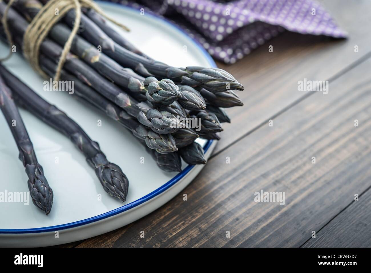 Un gambi commestibili e grezzi di asparagi su un vassoio su un chioseup di legno di fondo Foto Stock
