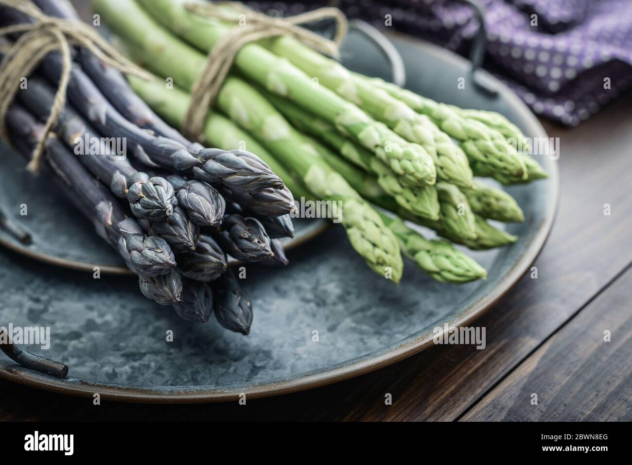 Un gambi commestibili e grezzi di asparagi su un vassoio su un chioseup di legno di fondo Foto Stock