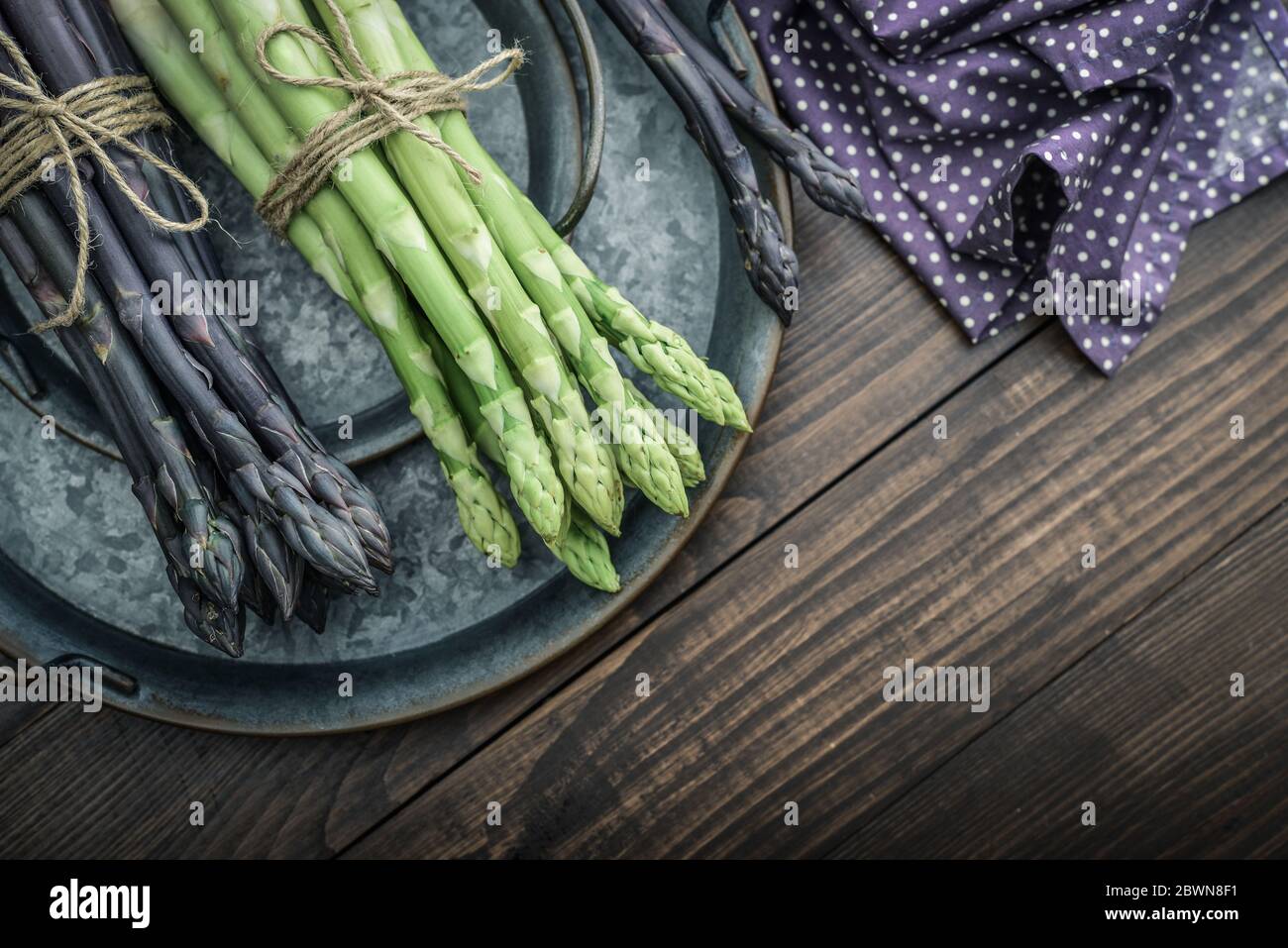 Un gambi commestibili e grezzi di asparagi su un vassoio su sfondo di legno, vista dall'alto Foto Stock
