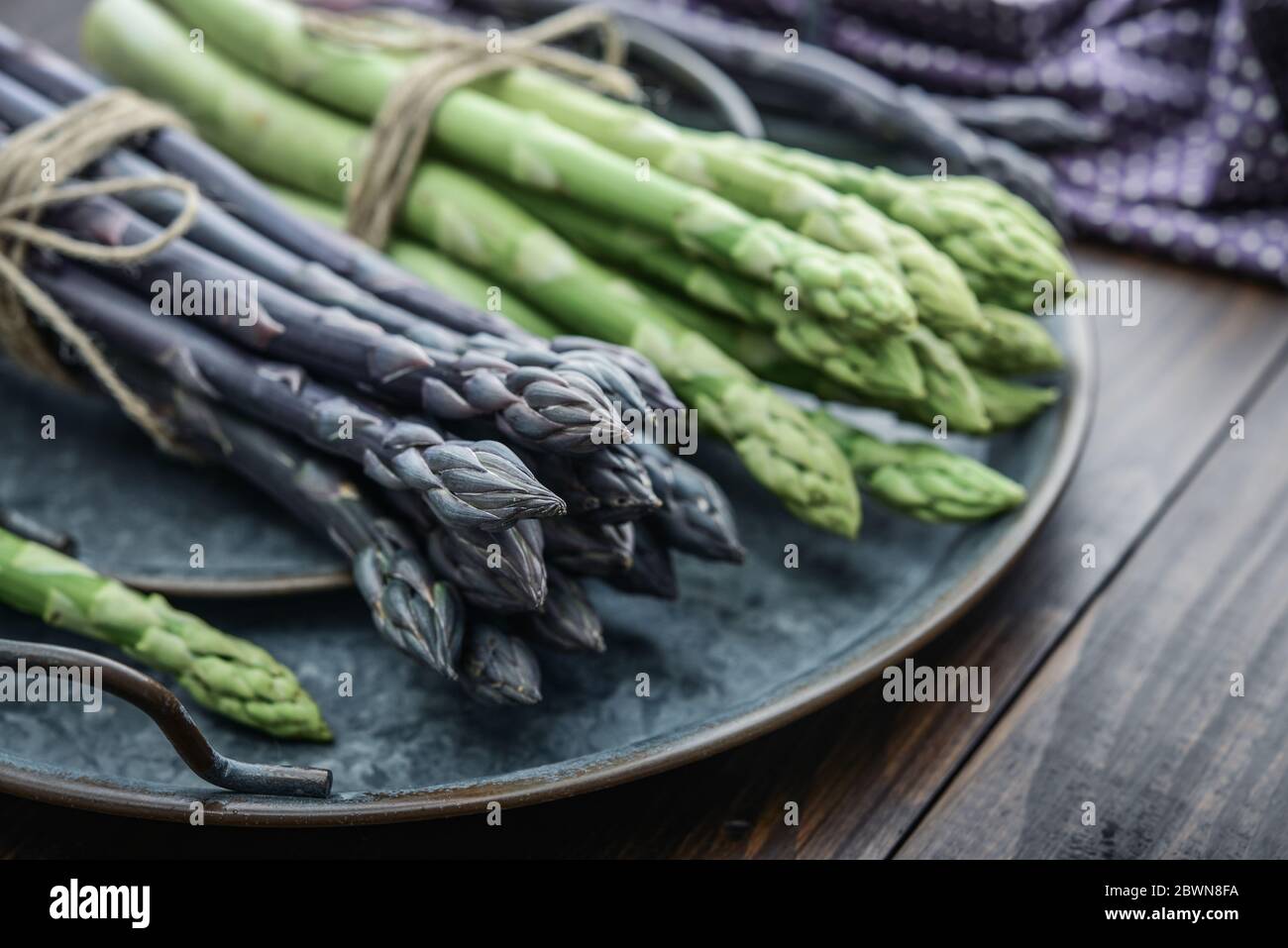 Un gambi commestibili e grezzi di asparagi su un vassoio su un chioseup di legno di fondo Foto Stock