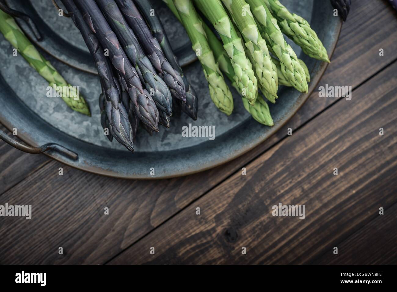 Un gambi commestibili e grezzi di asparagi su un vassoio su sfondo di legno, vista dall'alto Foto Stock