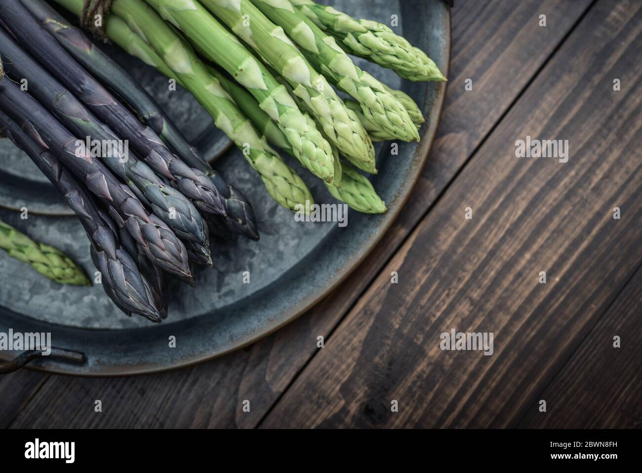 Un gambi commestibili e grezzi di asparagi su un vassoio su sfondo di legno, vista dall'alto Foto Stock