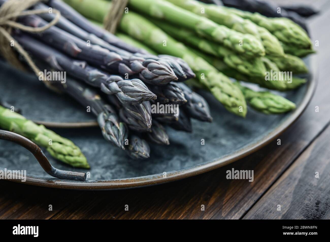 Un gambi commestibili e grezzi di asparagi su un vassoio su un chioseup di legno di fondo Foto Stock