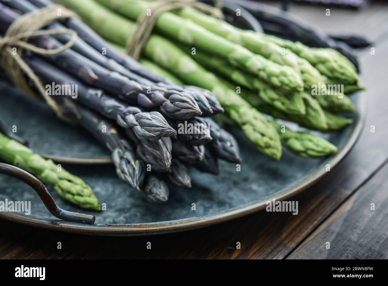 Un gambi commestibili e grezzi di asparagi su un vassoio su un chioseup di legno di fondo Foto Stock