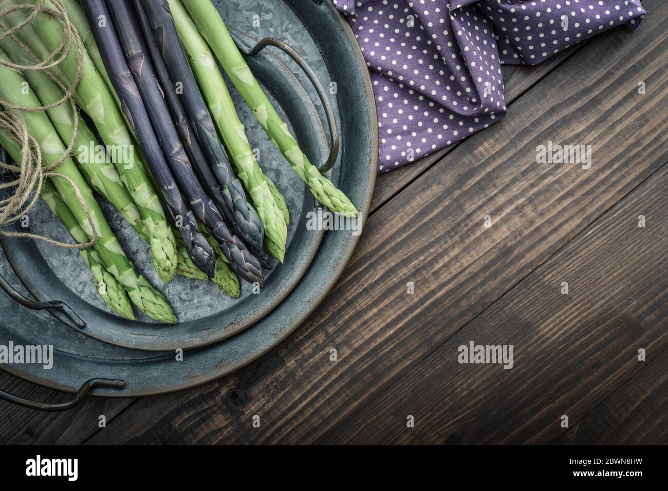 Un gambi commestibili e grezzi di asparagi su un vassoio su sfondo di legno, vista dall'alto Foto Stock