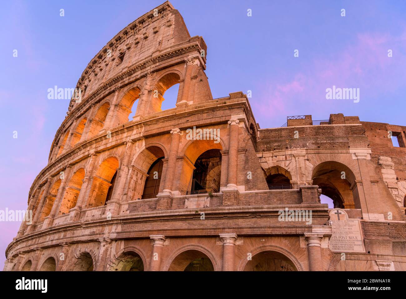 Tramonto Colosseo - Vista ravvicinata del tramonto sulla parte superiore della parete esterna ovest del Colosseo, con due placche in marmo inscritto latino. Roma, Italia. Foto Stock