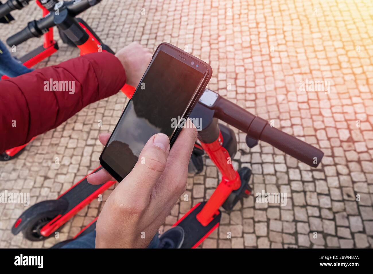 Uomo che tiene un telefono vicino al moderno scooter elettrico della città, andando a sbloccarlo. Foto Stock