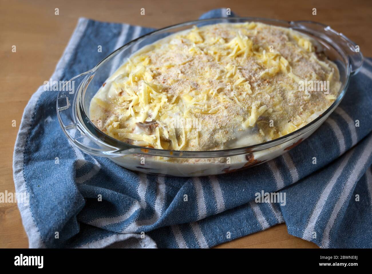 Moussaka preparato pronto per cuocere in forno, una tradizionale casseruola greca di melanzane, patate, carne macinata e salsa in una muffa di vetro su un ki blu Foto Stock