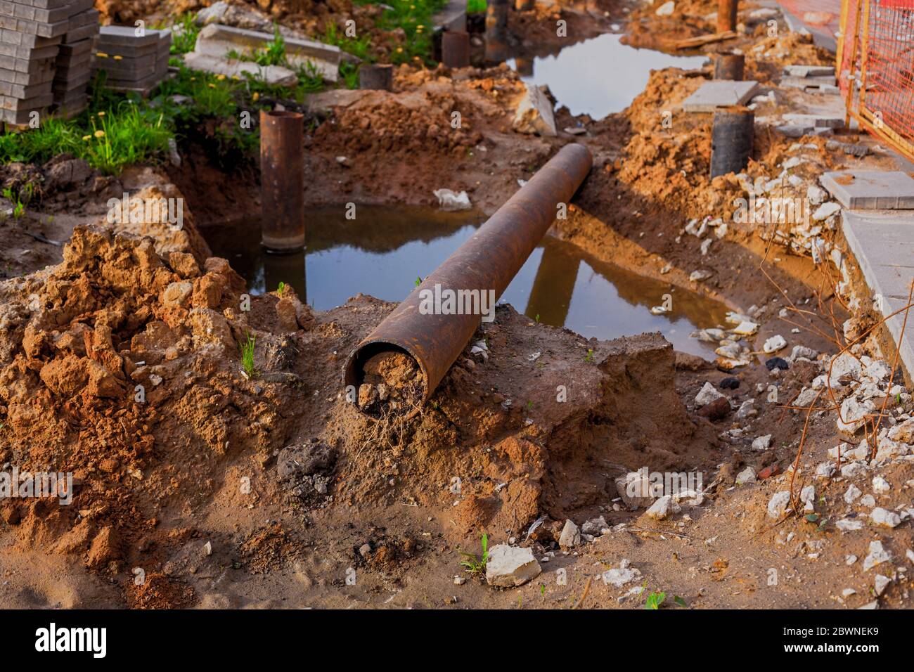 Tubo di metallo che posa sul terreno sopra la pozza. Lavori di ricostruzione Foto Stock