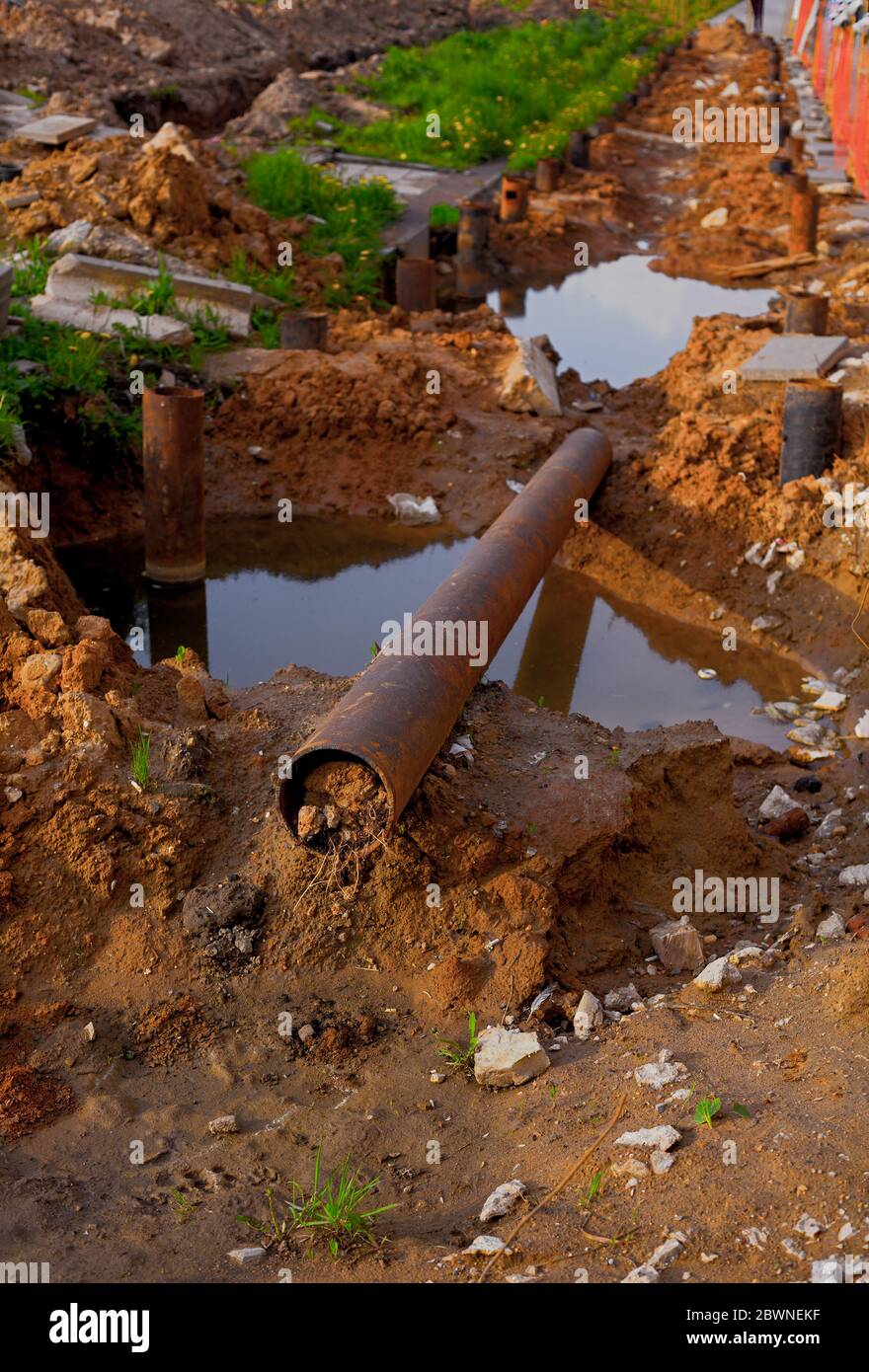 Tubo di ferro arrugginito che posa in fango. Lavori di costruzione. Shot verticale Foto Stock