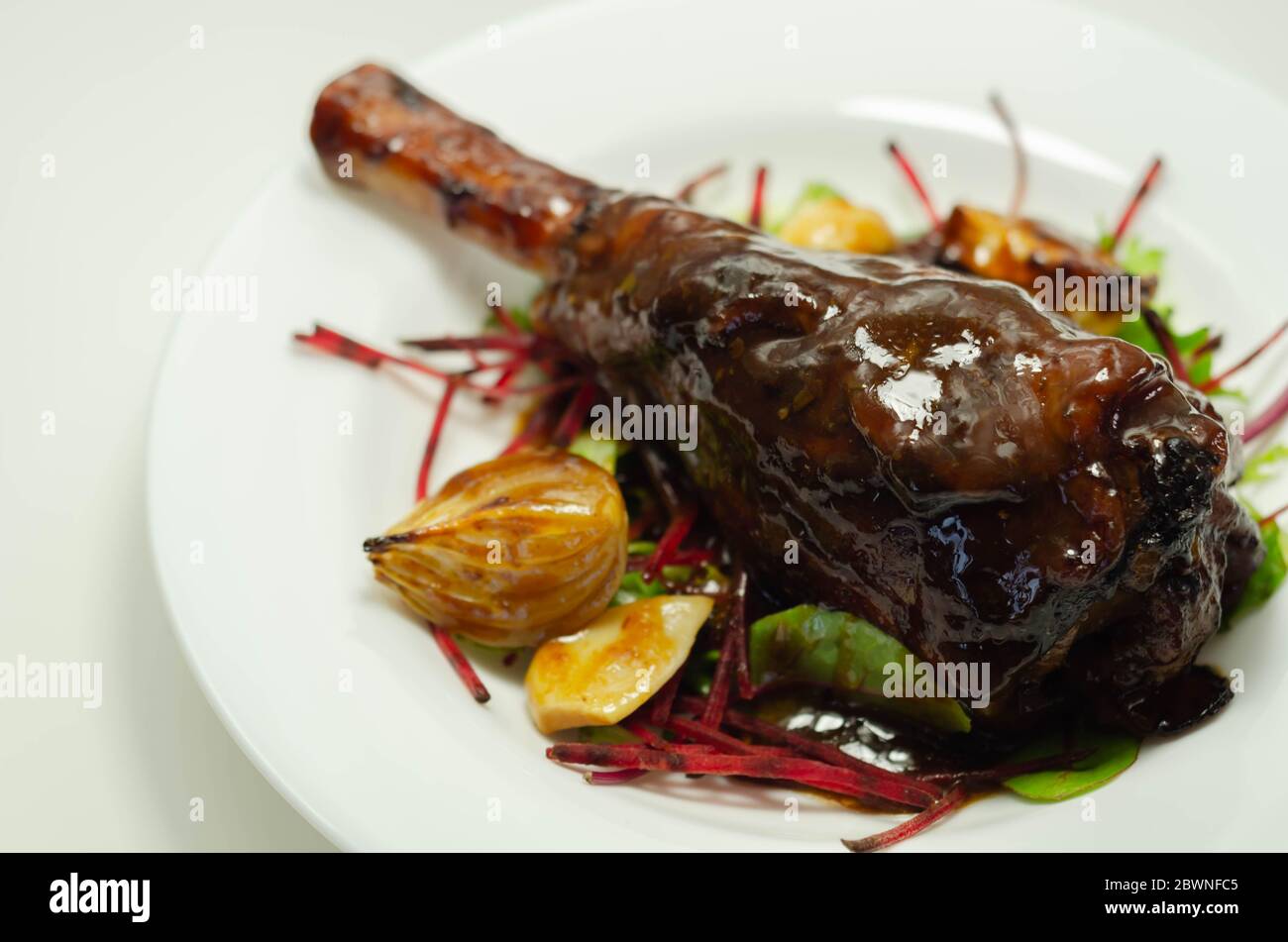 Delizioso gambo di agnello con vino rosso e salsa di rosmarino servito sull'insalata mista a foglie, piatto esclusivo Foto Stock