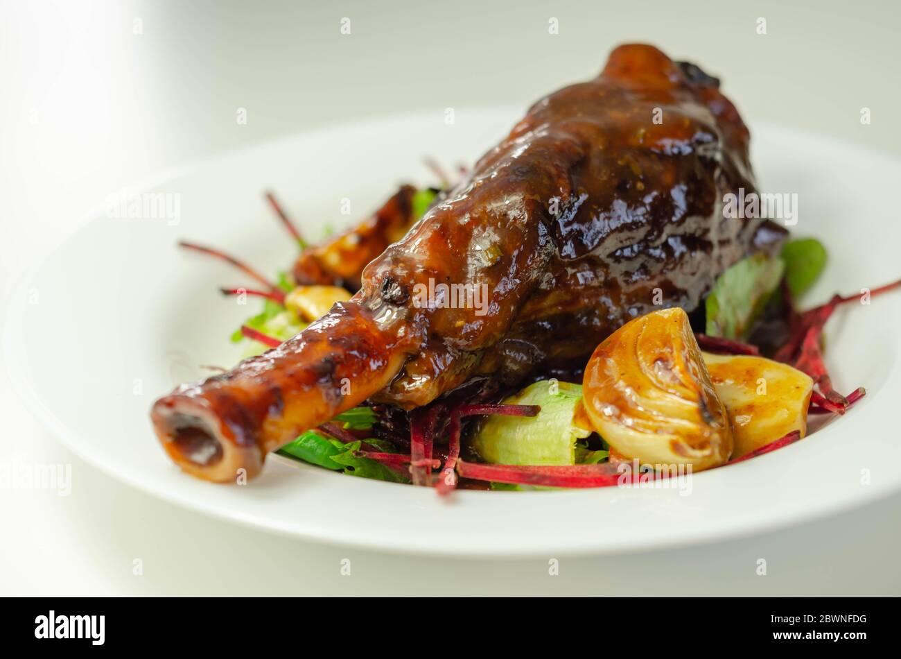 Delizioso gambo di agnello con vino rosso e salsa di rosmarino servito sull'insalata mista a foglie, piatto esclusivo Foto Stock