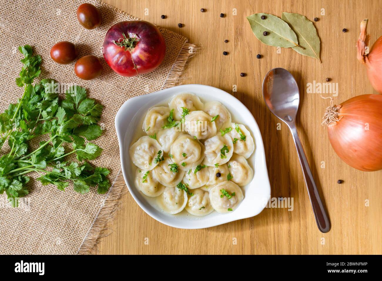 Ciotola di gustosi gnocchi in brodo, servita su tavola di legno, con verdure fresche intorno. Vista dall'alto. Foto Stock