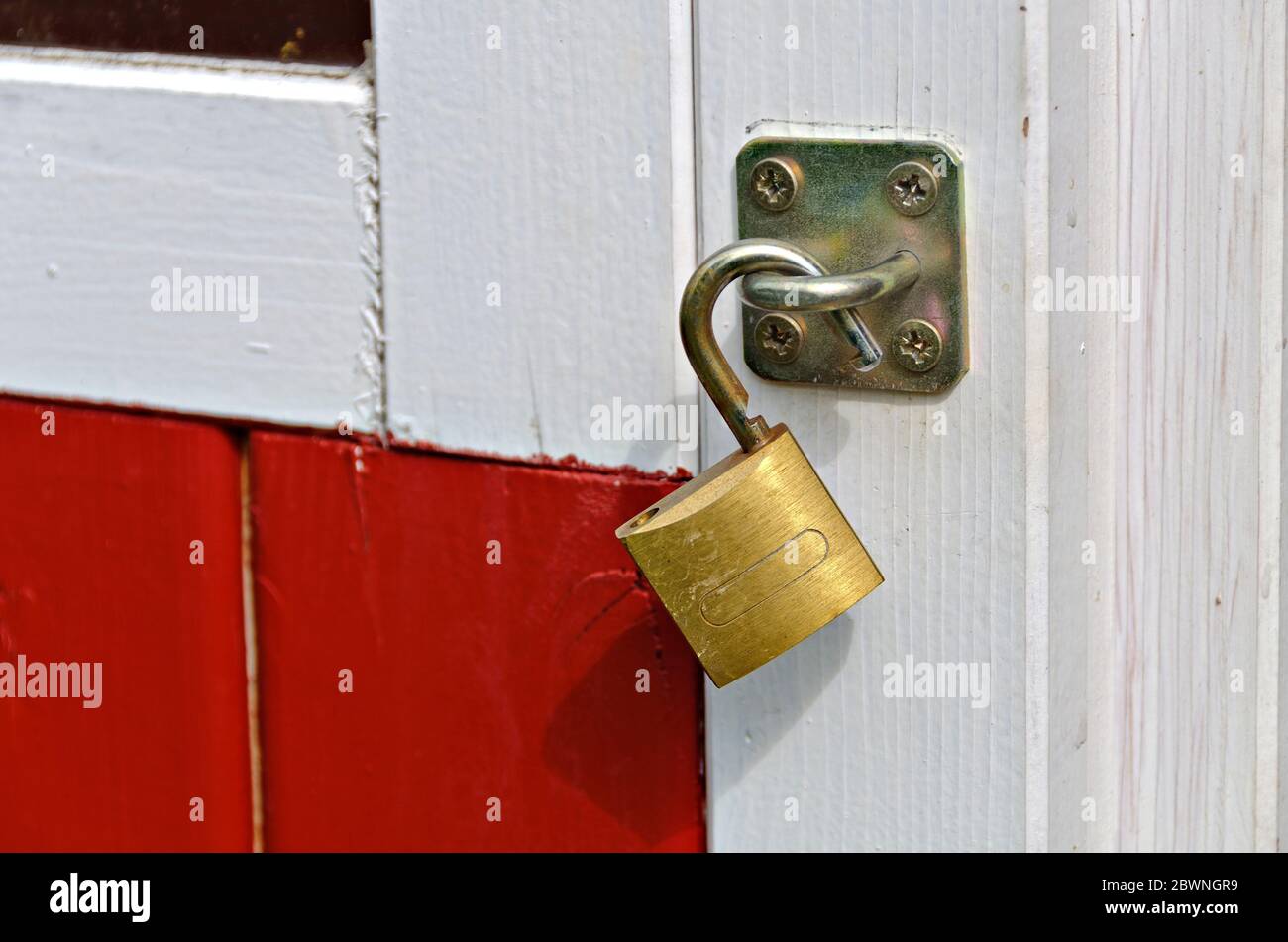lucchetto in ottone colorato su una porta dipinta di rosso e bianco di una casa in legno Foto Stock