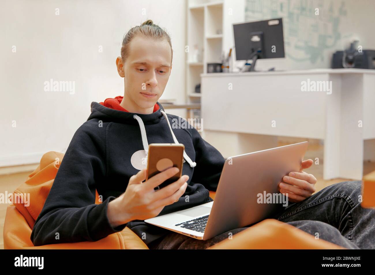 Un giovane si siede in una poltrona e lavora su un computer. Foto Stock