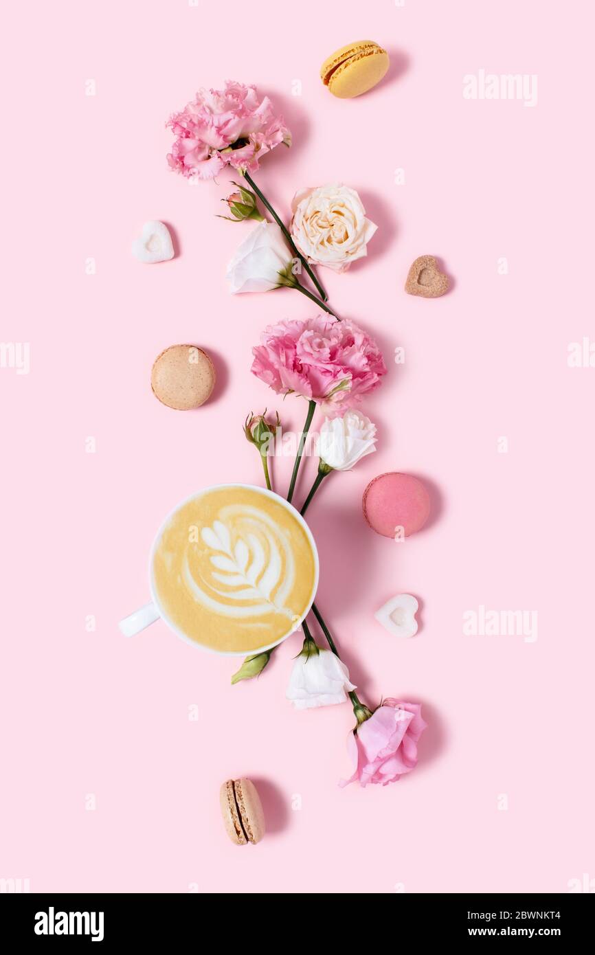 Delizioso cappuccino in fiori e macaroon su sfondo rosa. Mattina emozioni positive. Foto Stock