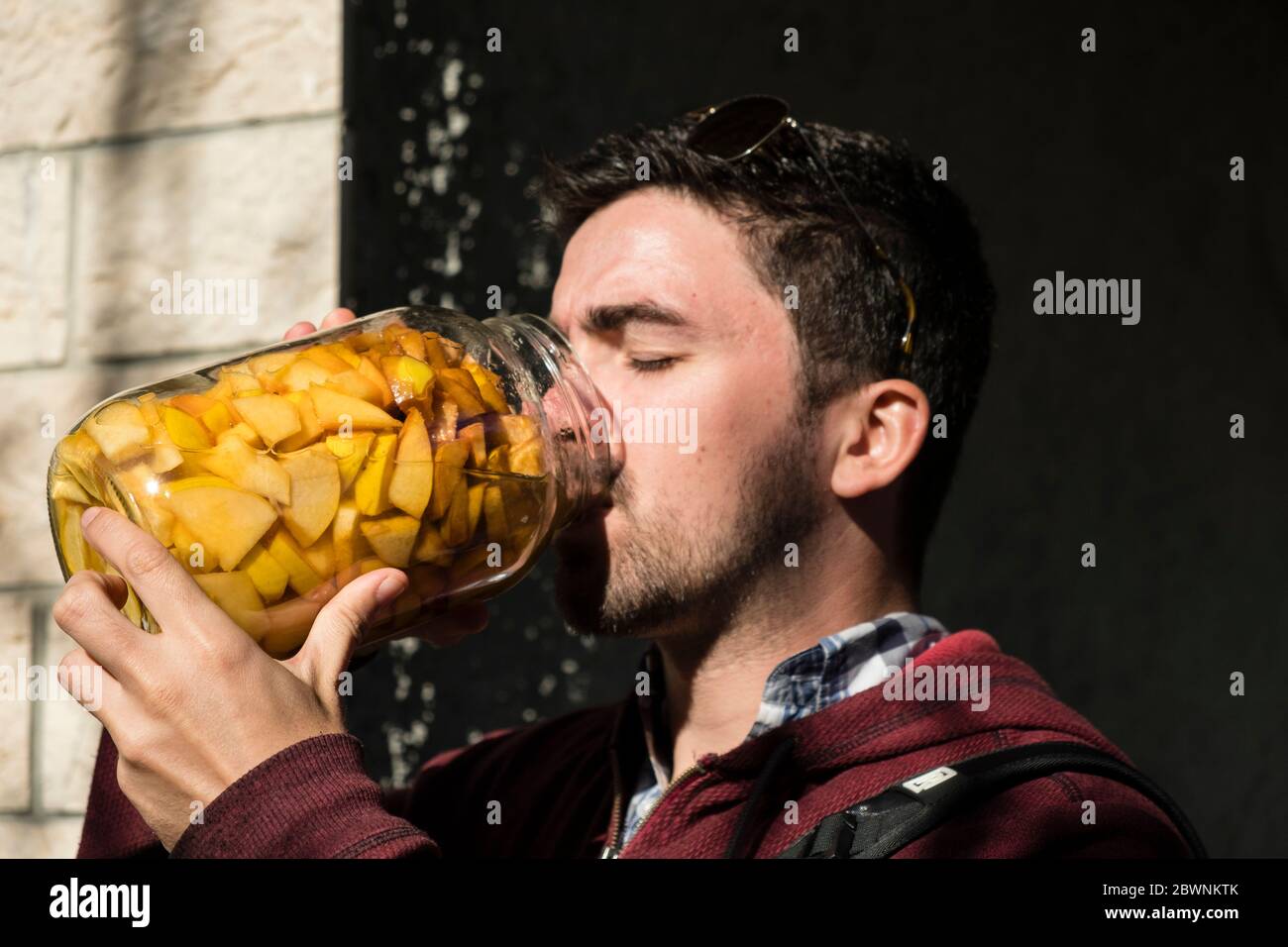 L'uomo prende una bevanda da un grande vaso di vetro riempito con frutta conservata e succo. Foto Stock