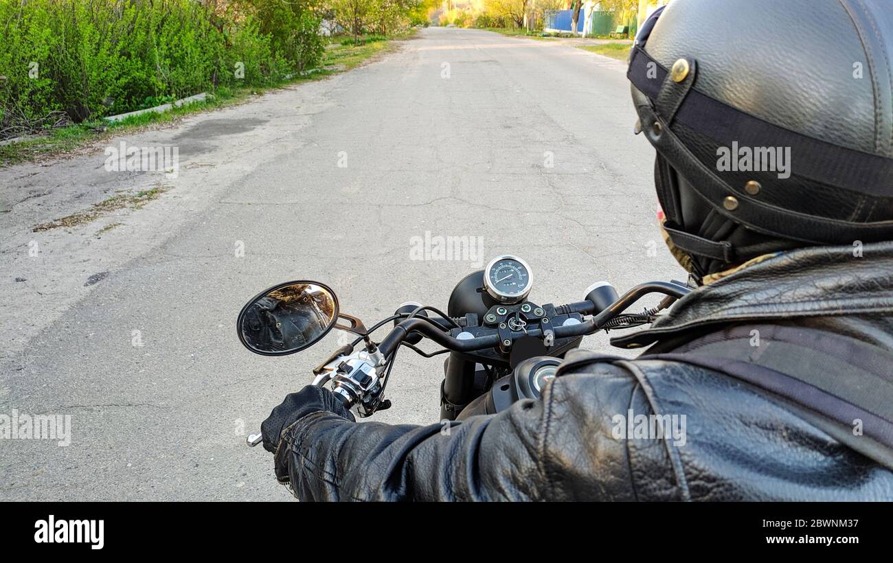 Motociclista che indossa un casco. Vista in prima persona su una moto che corre sulla strada del villaggio, vista sulla strada Foto Stock