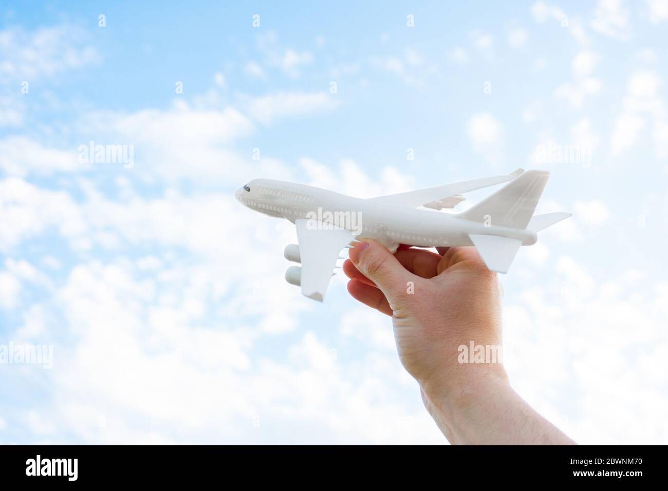 Gioca con un aeroplano giocattolo in mano su cielo con le nuvole. Volo di ispirazione di viaggio aereo che tiene la mano. Foto Stock