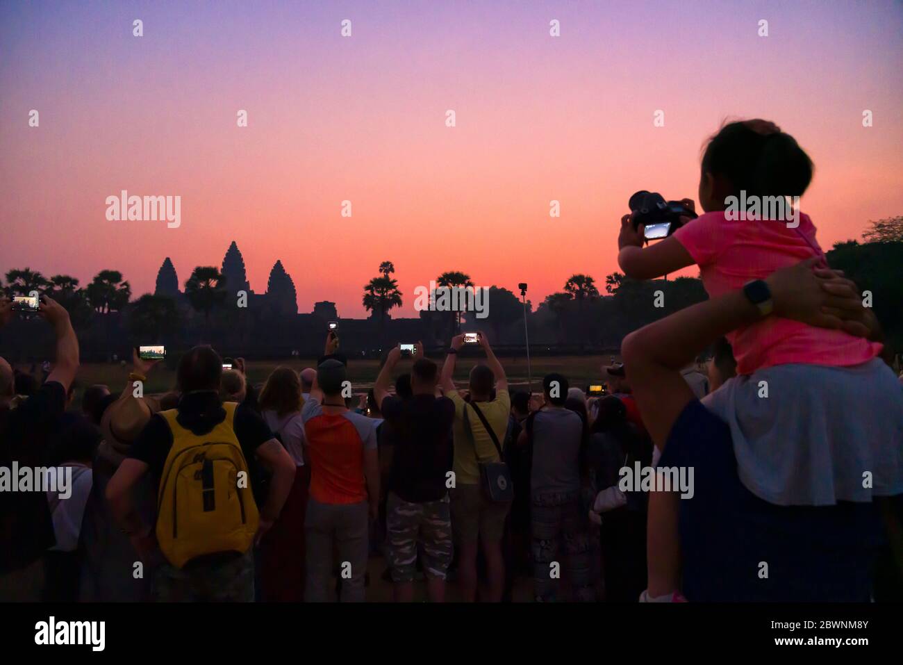Il turista stimola il bambino sulle spalle per una migliore foto dell'alba a Angkor Wat, come molti turisti scattano foto al telefono all'alba. Foto Stock