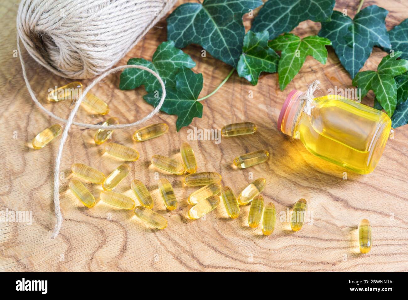 Capsule gelatinose trasparenti di olio di pesce sono state sparse sullo sfondo di legno vicino alla bottiglia di olio. Acidi grassi polinsaturi Omega-3-essenziali Foto Stock