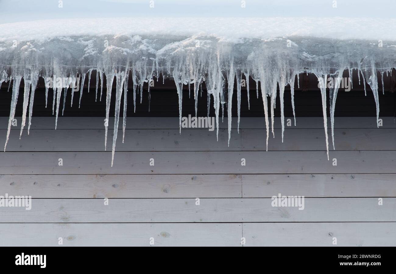 Edificio coperto di icicles, guardaroba. Stalattite di ghiaccio appesa al tetto, spazio di copia. Un isolamento termico scadente del tetto provoca la formazione di ic Foto Stock