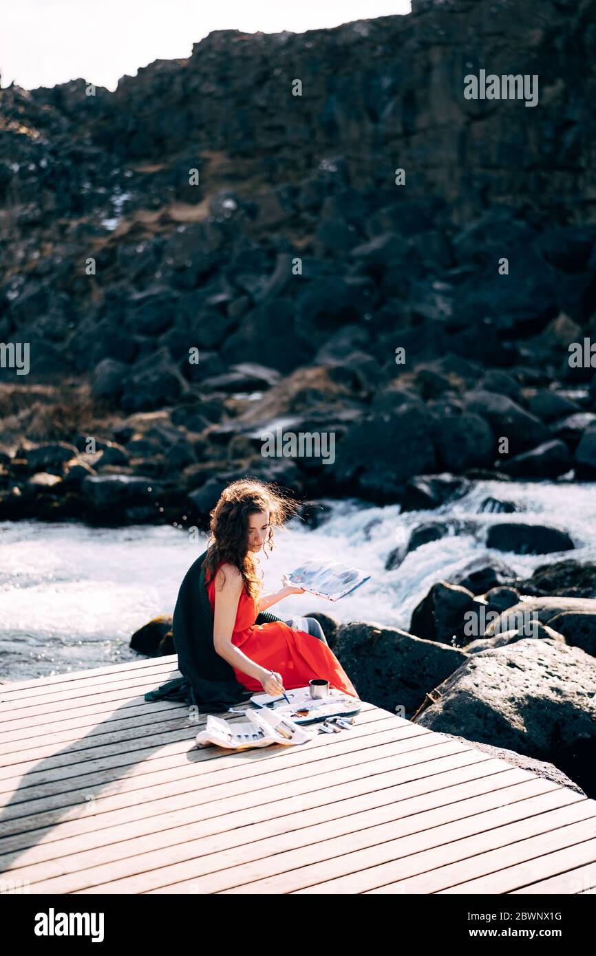 L'artista della ragazza dipinge una foto dell'album con acquerelli. Vicino alla cascata di Ehsaraurfoss, al fiume Ehsarau, al Parco Nazionale di Thingvedlir in Islanda. Foto Stock
