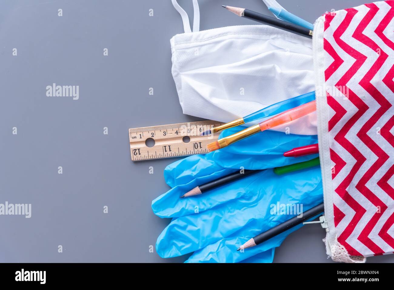 Primo piano della custodia a matita per bambini con materiale scolastico, maschera medica e guanti chirurgici che fuoriescono sulla scrivania Foto Stock