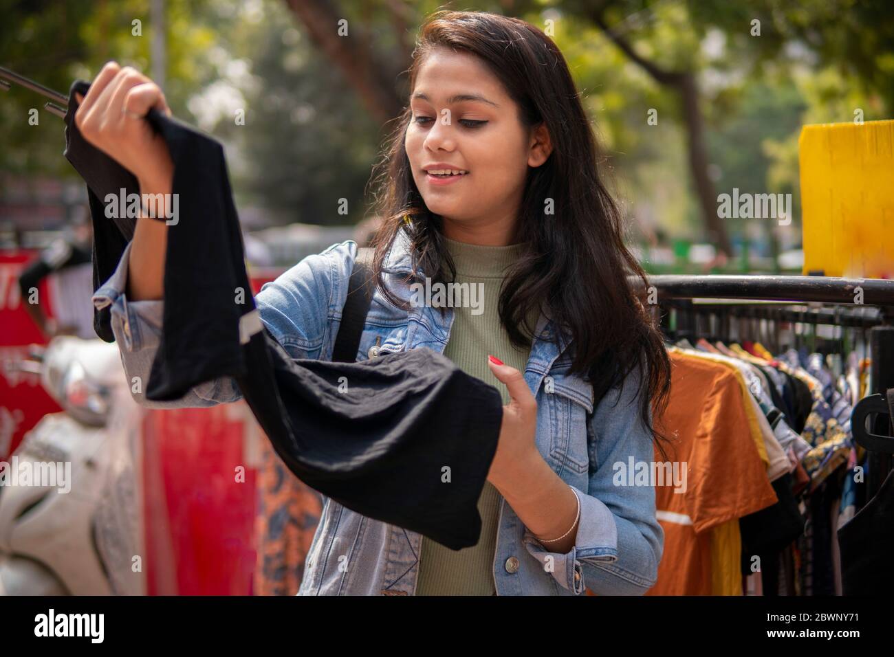 Felice ragazza teen tarda che osserva e che compra i vestiti dal mercato esterno della strada di Delhi, India al giorno. Foto Stock