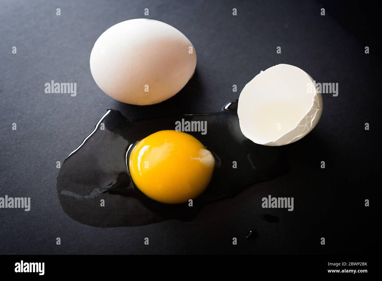 immagine orizzontale bassa chiave di un uovo organico grezzo spaccato su uno sfondo nero. Foto Stock