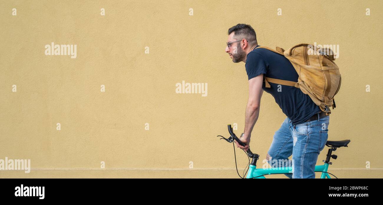 giovane trendy che posa su una bicicletta minimalista, ritratto di un ciclista in un contesto urbano, in bicicletta in città per andare a lavorare con il suo zaino, conce Foto Stock